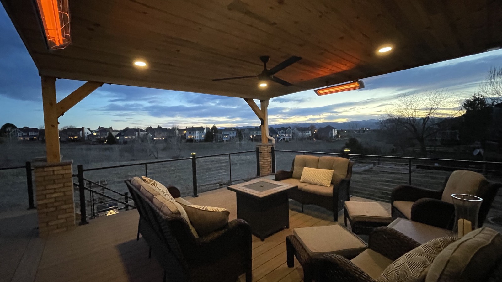 A covered Tekton deck at dusk, warm lighting under a timber roof, looking out over the Colorado Front Range.